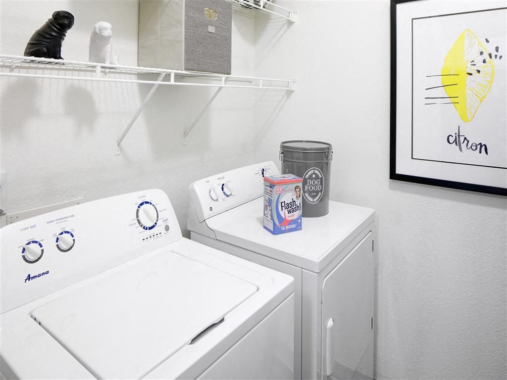Laundry room with a washer and dryer, a shelf above, and laundry supplies on the machines.