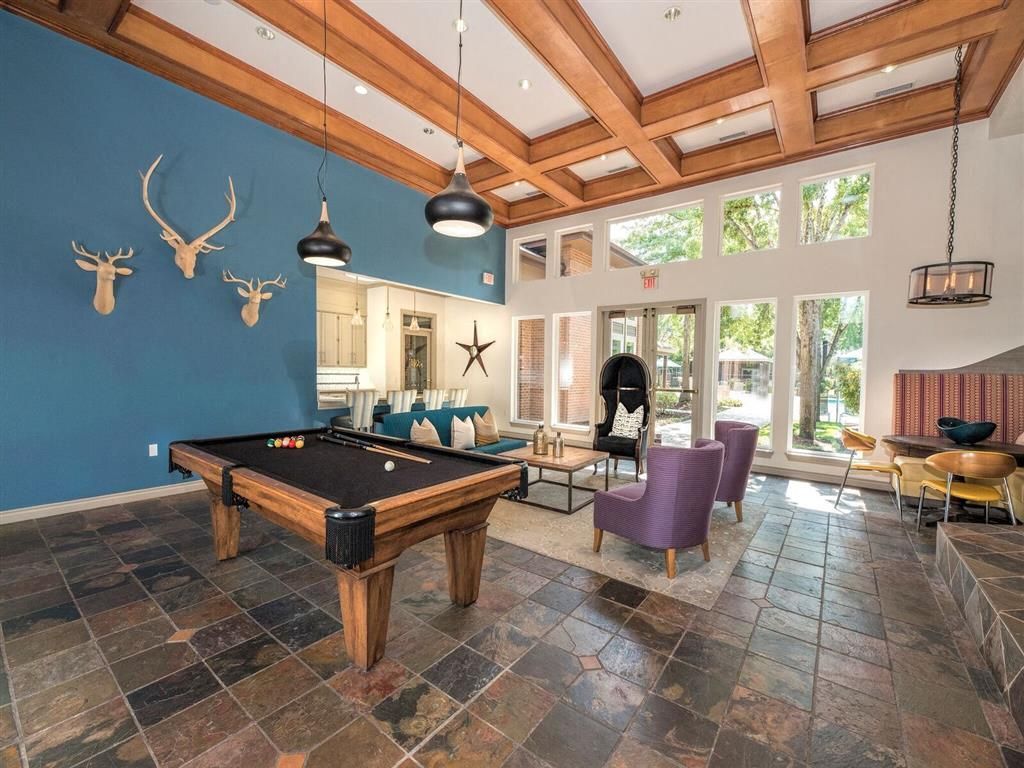 Interior of a community lounge with a pool table, seating area, and large windows.