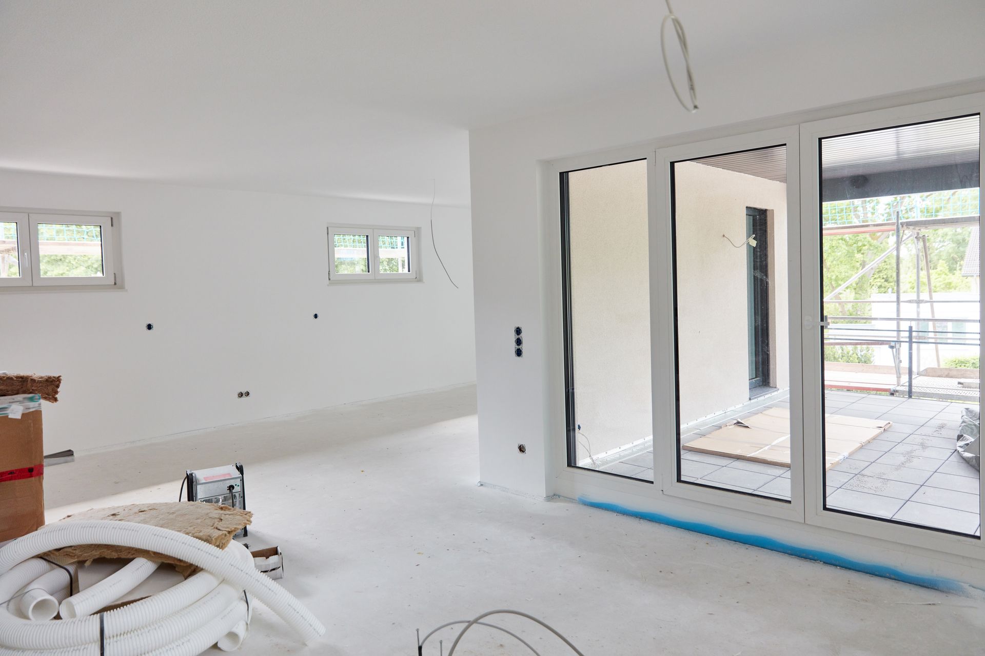 A modern room under construction with white walls, multiple windows, a large glass sliding door.