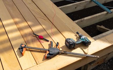 Construction tools, including a drill and a clamp, resting on wooden deck planks currently under construction.