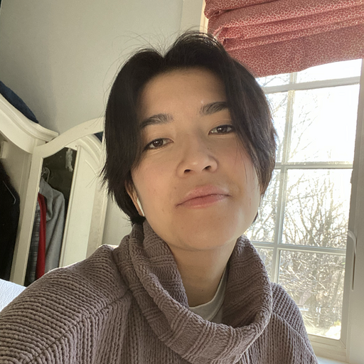 Person with short, dark hair wearing a mauve sweater, near a window and a white closet.