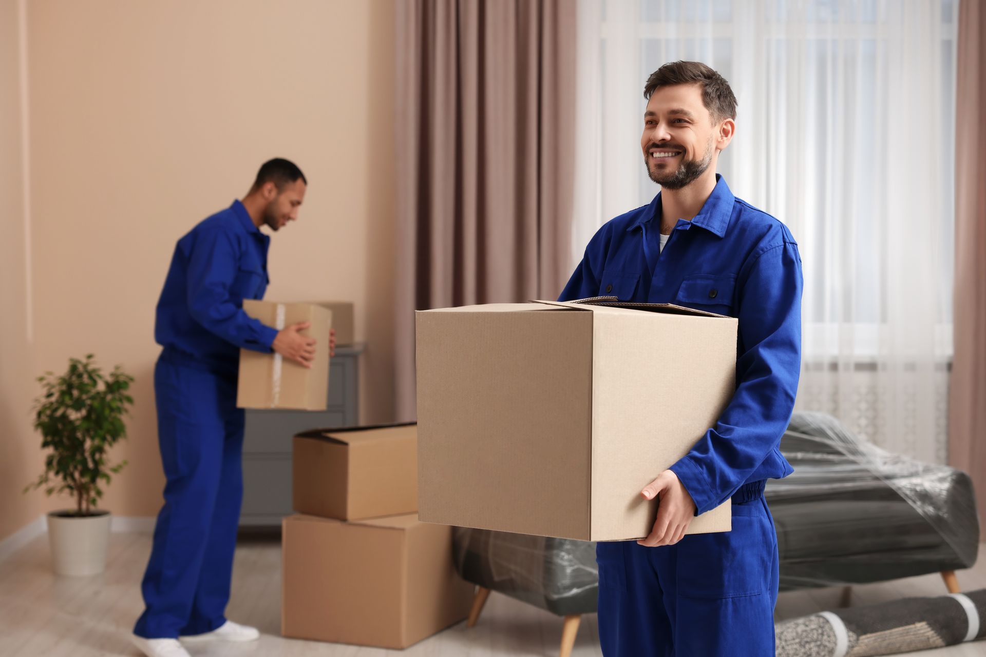 Two men are carrying boxes in a living room.
