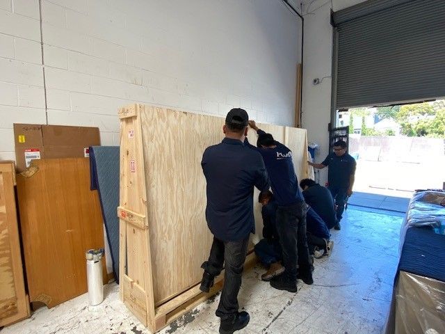 A group of men are working on a large wooden crate in a warehouse.
