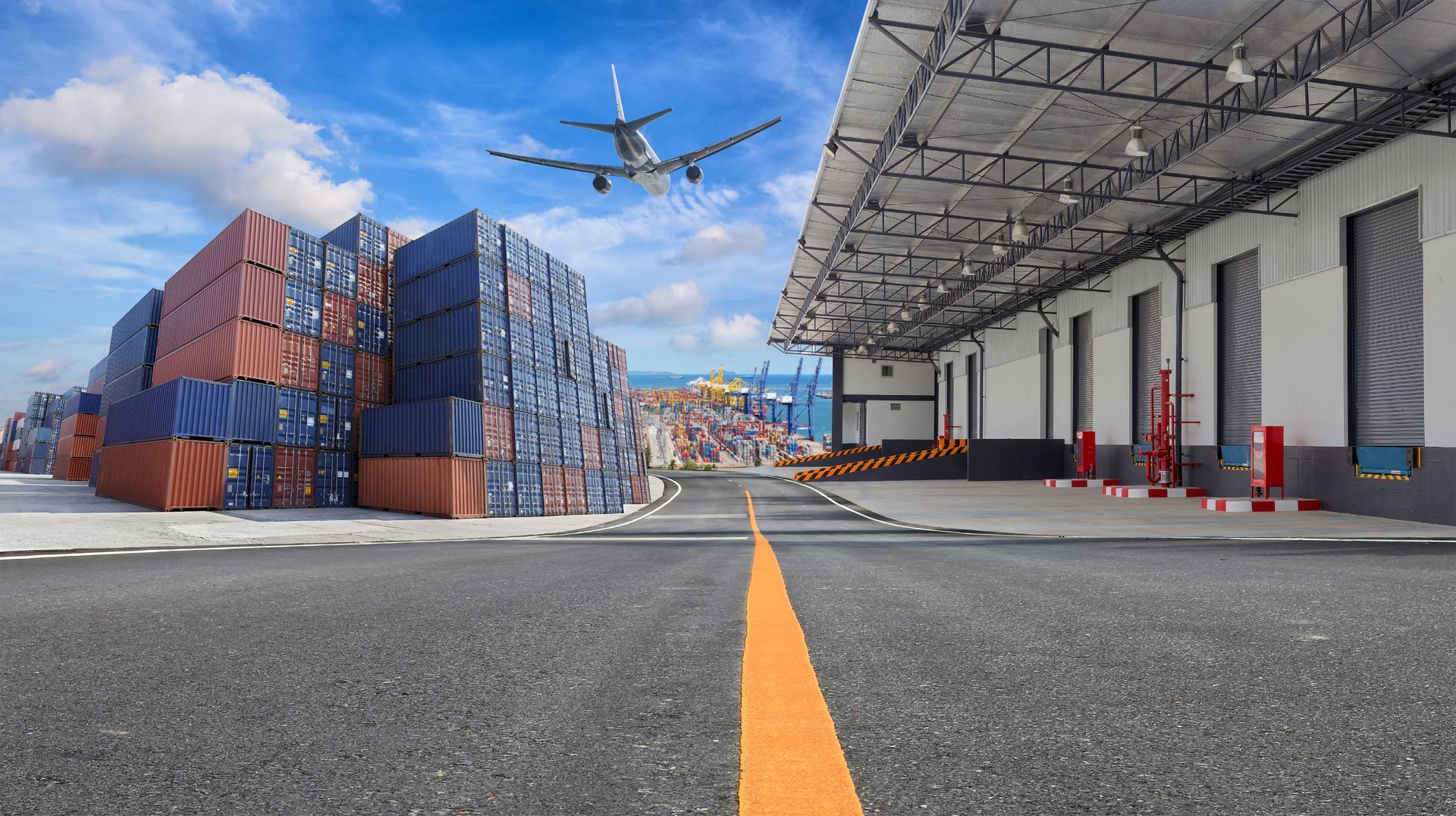 Shipping containers stacked near a warehouse and runway, plane overhead, blue sky, ocean in the distance.