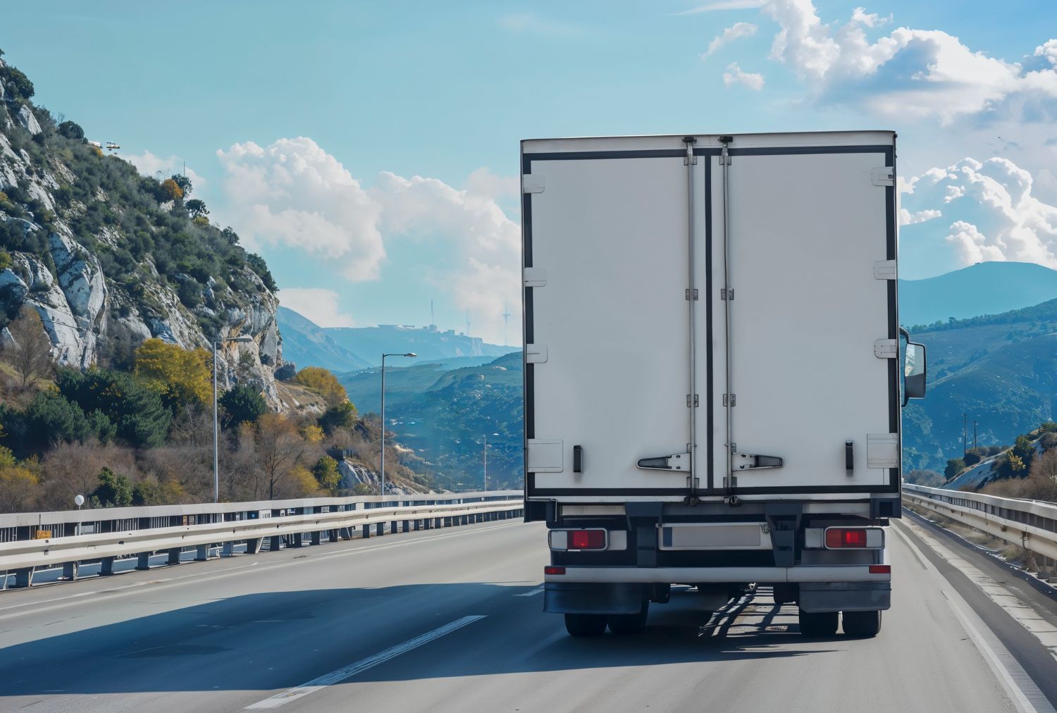 White truck on a highway, mountains in the background, blue sky.