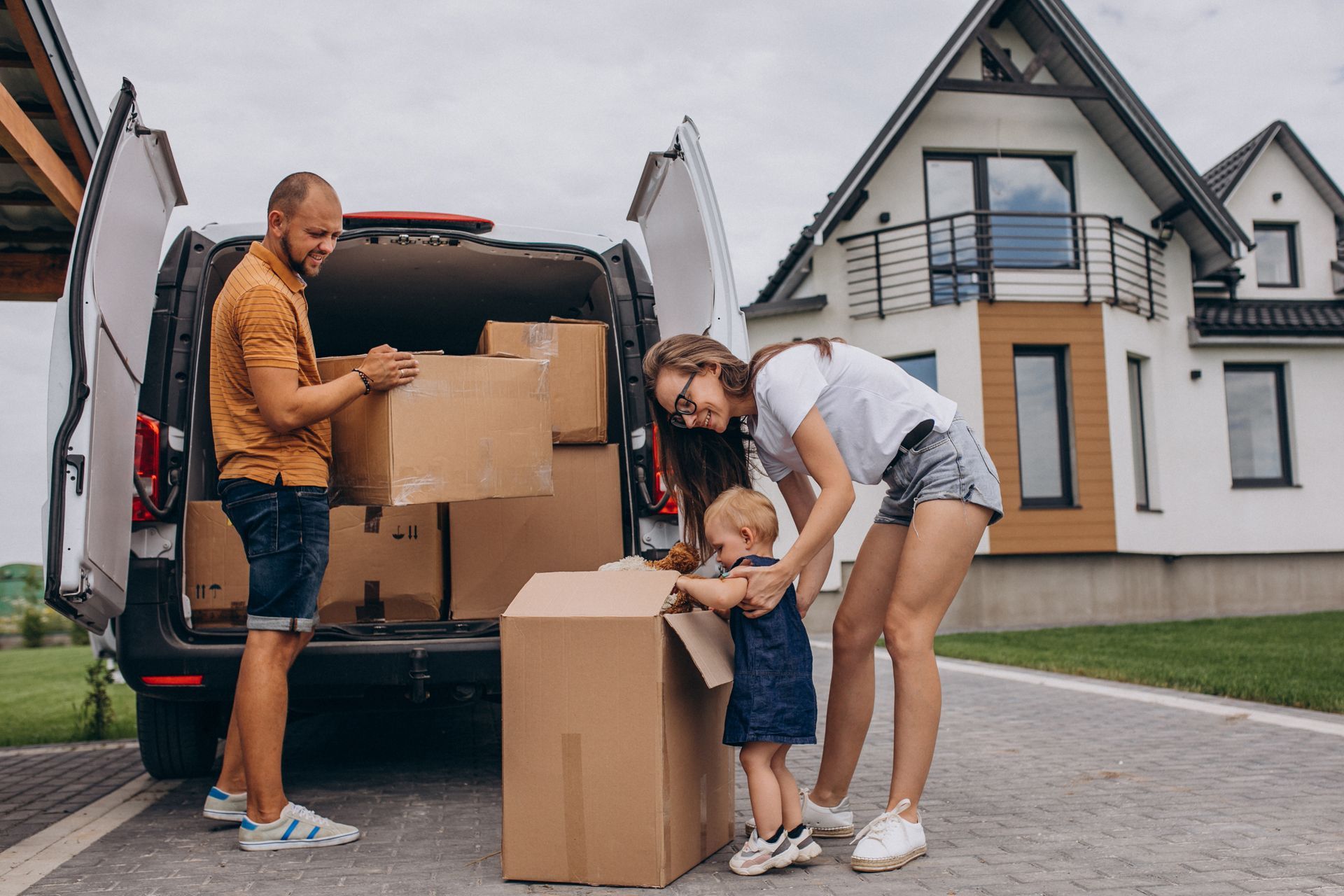 Family unpacking boxes from a van in front of a new house.