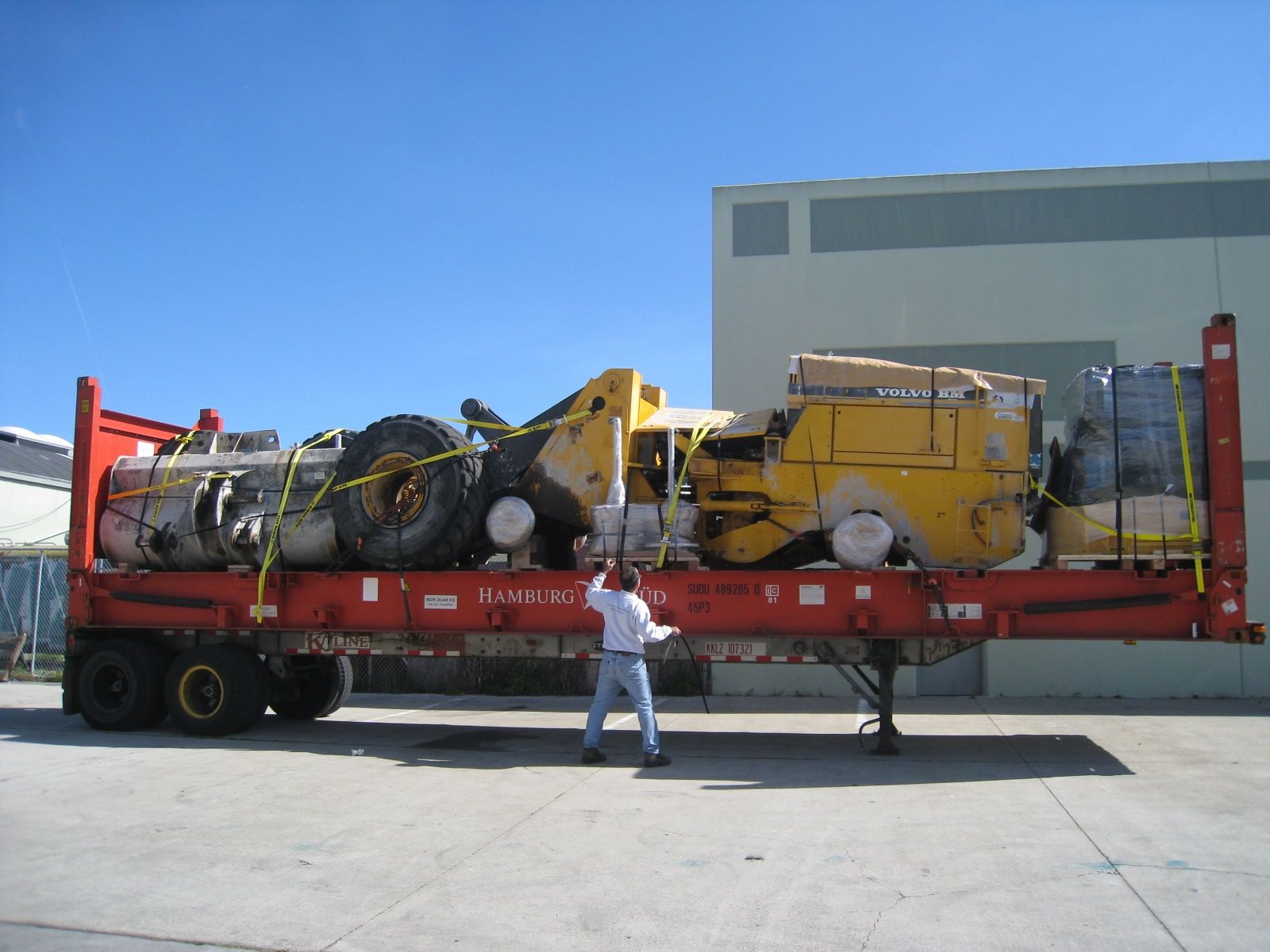 A man is pushing a large yellow truck on a red trailer