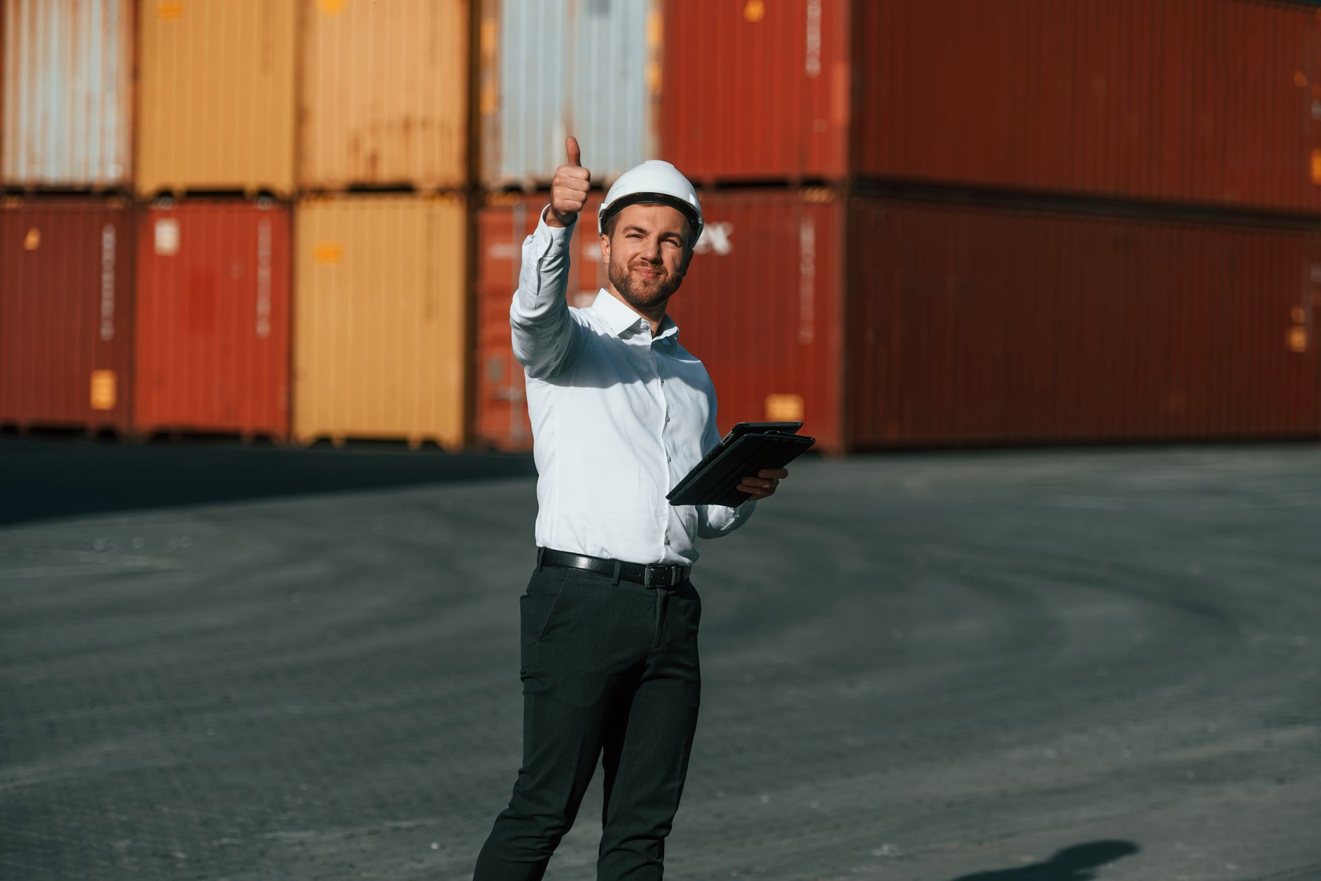 A man in a hard hat is holding a clipboard and giving a thumbs up.
