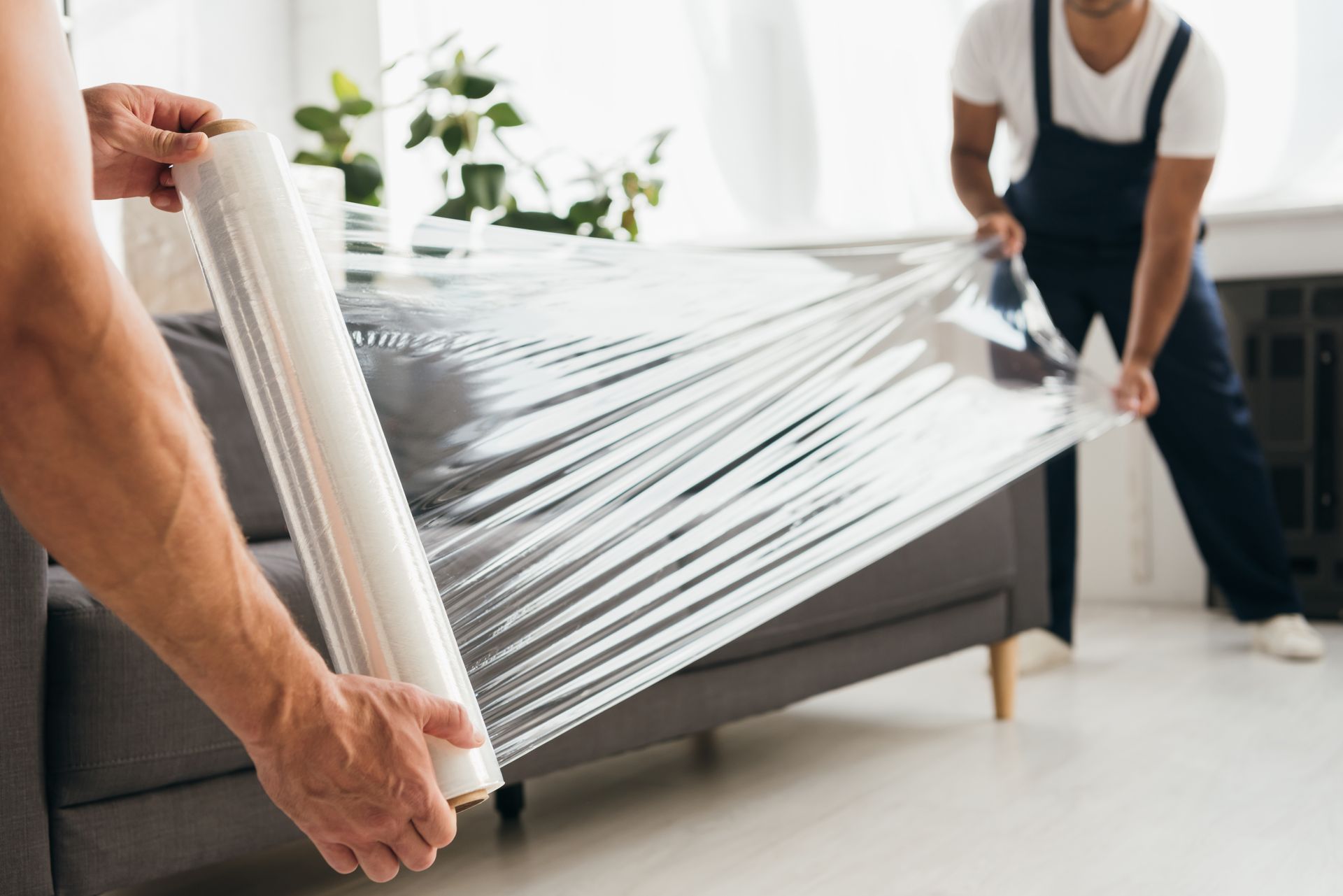 A man is holding a roll of plastic wrap in front of a couch. Stress-free, secure  home movers.