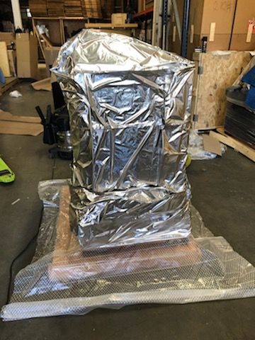 A large piece of metal wrapped in aluminum foil is sitting on top of a wooden table in a warehouse.