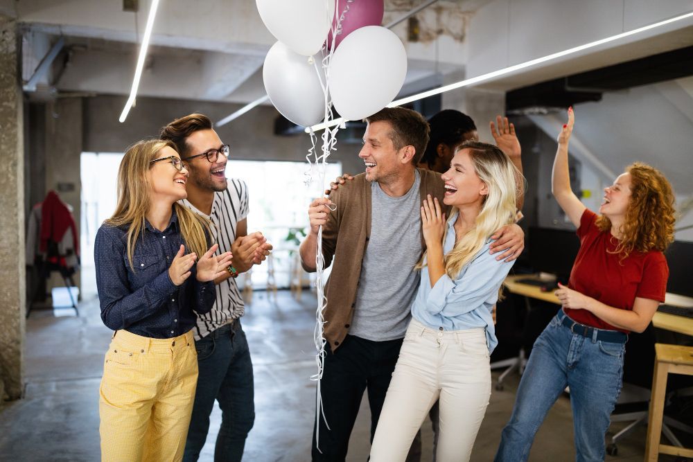 Un groupe de personnes fête un anniversaire dans un bureau avec des ballons.