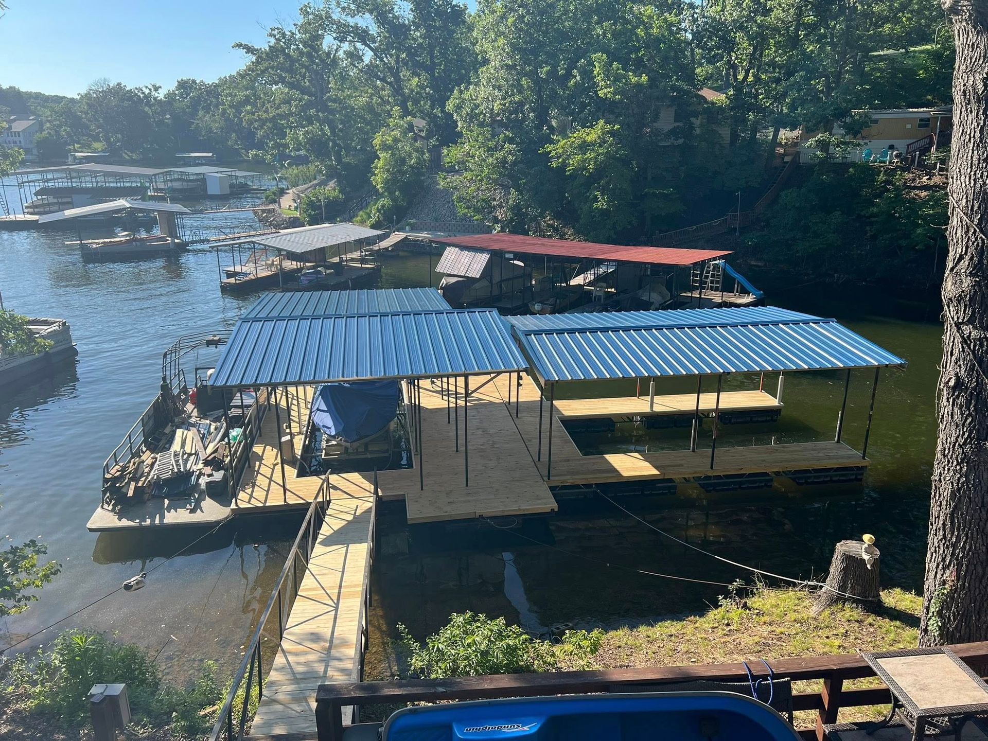 Docks with blue and red roofs on a lake surrounded by trees; sunny day.
