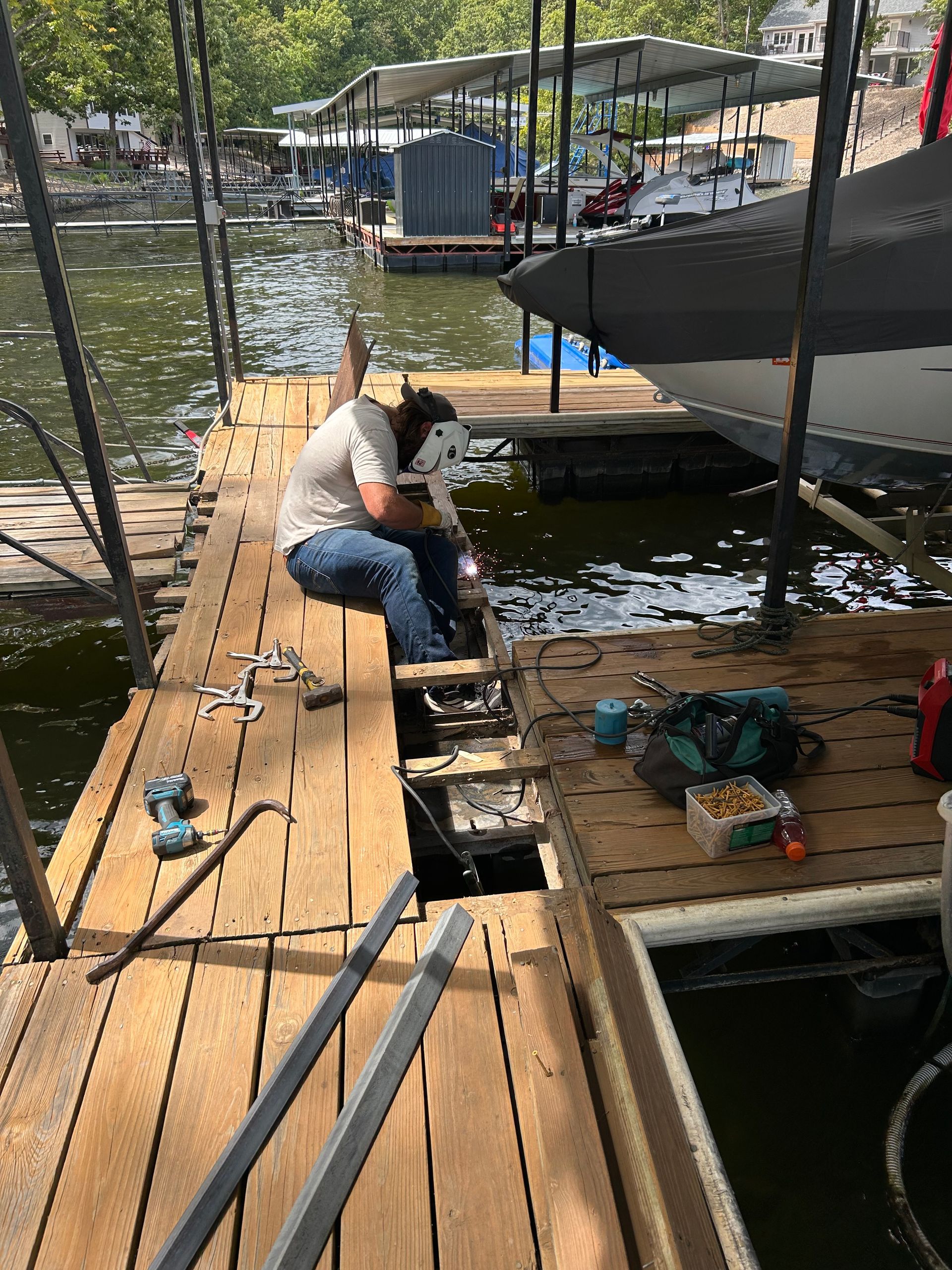 Man welding dock repairs on wooden pier near water.
