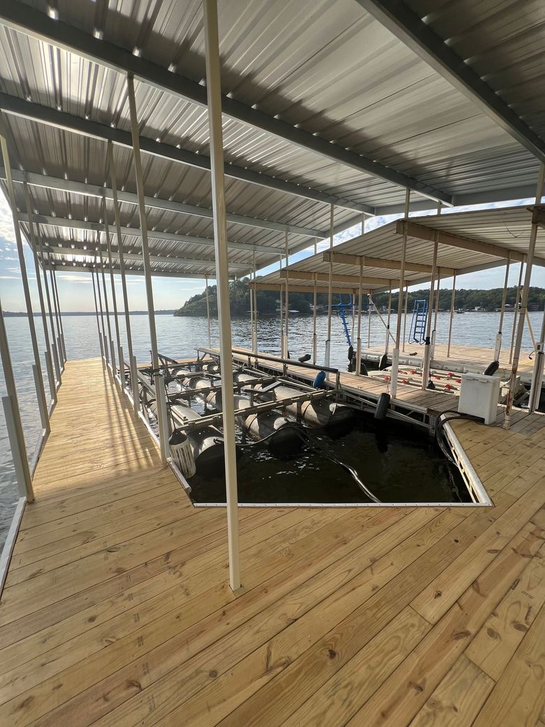 Dock with a metal roof over boat slips on a lake. Wooden deck in foreground.