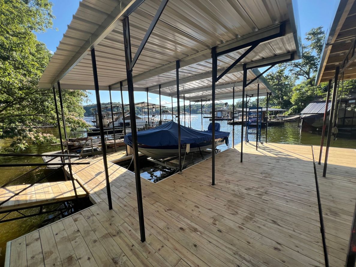 Dock with boat covered by a blue tarp, under a metal roof, on a lake.