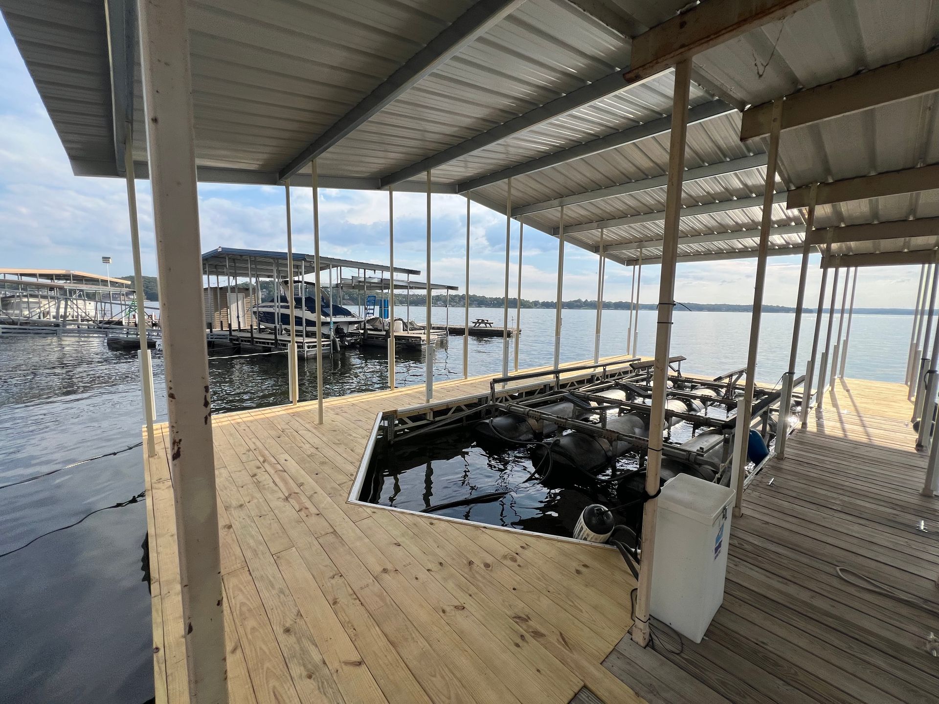 Wooden dock on a lake with covered boat slips. Clear water, overcast sky.