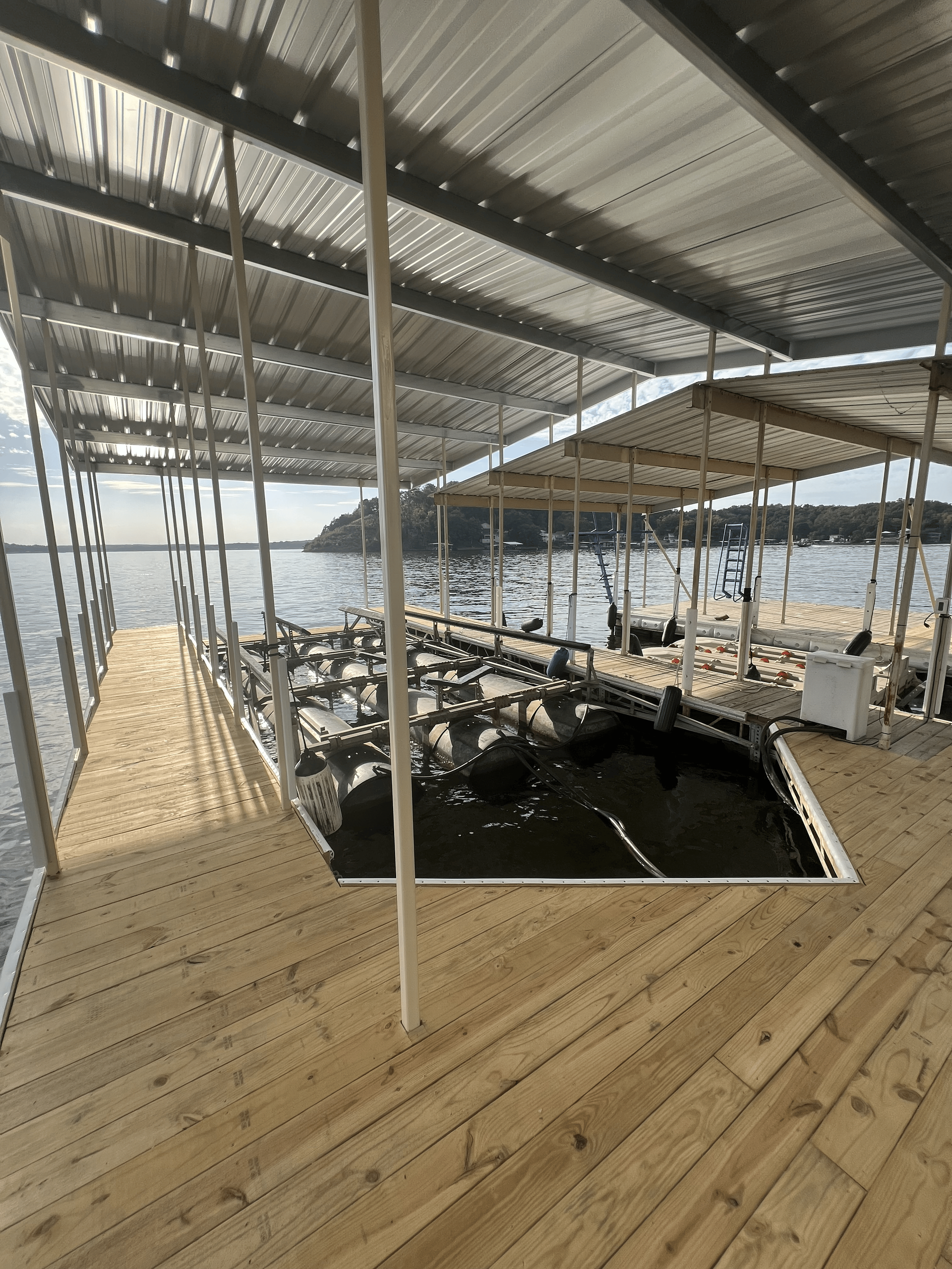 Wooden dock with metal roof and boat slips on a lake.