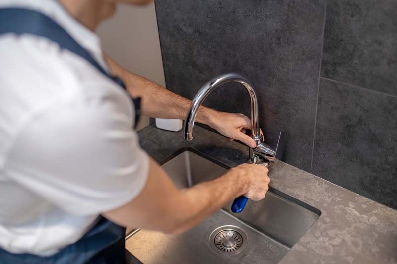 A man is fixing a faucet in a kitchen sink.