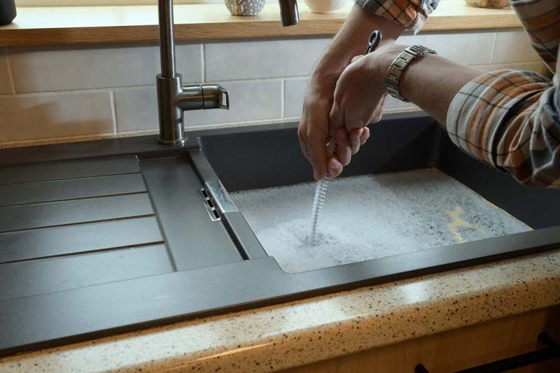 A person is cleaning a kitchen sink with a brush.