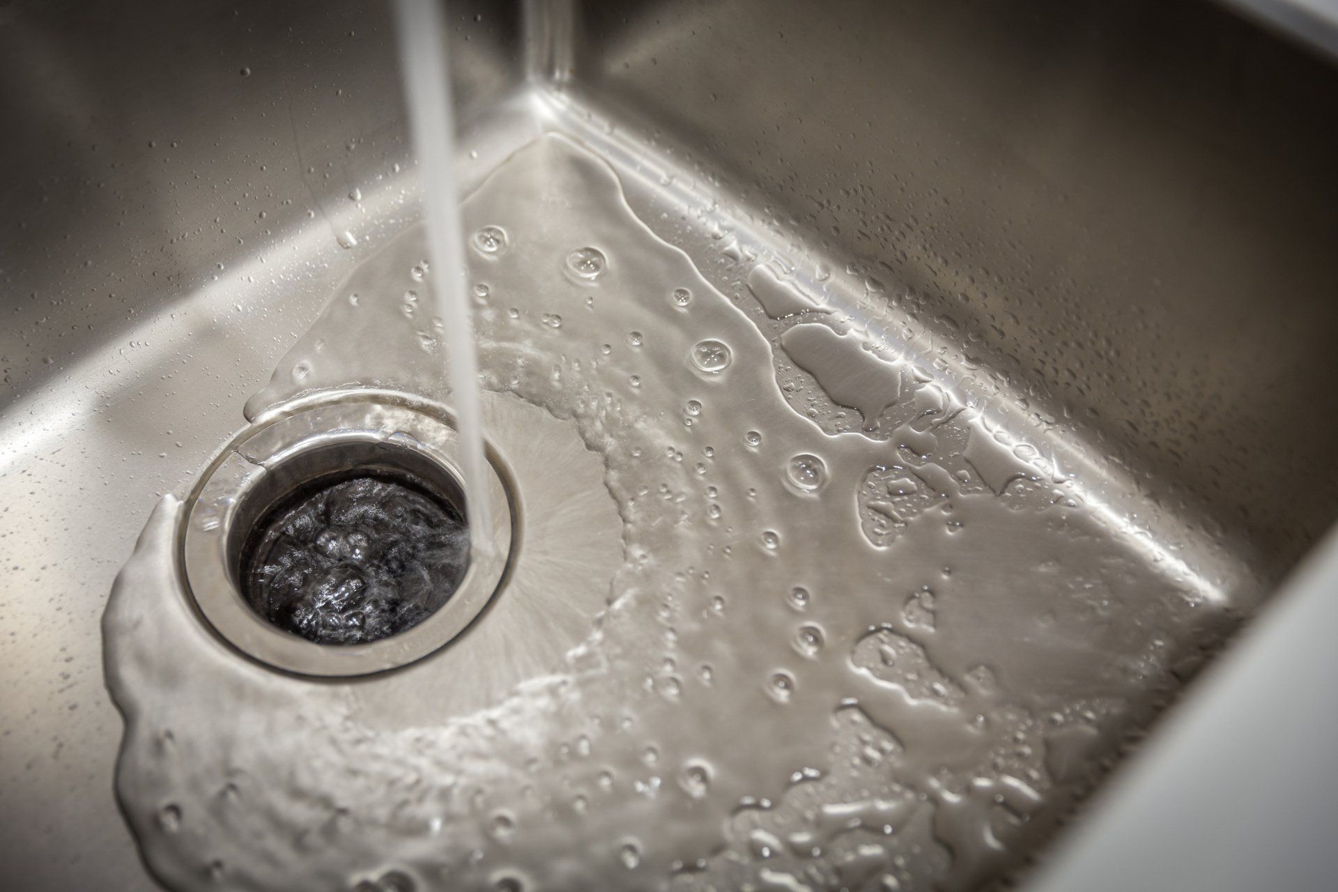 Water is running into a stainless steel kitchen sink.