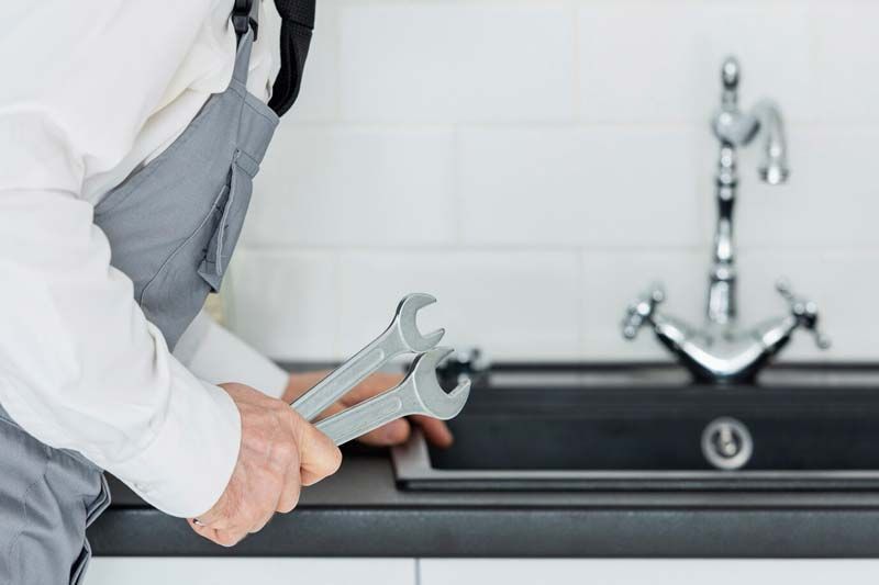 A plumber is fixing a sink with a wrench.