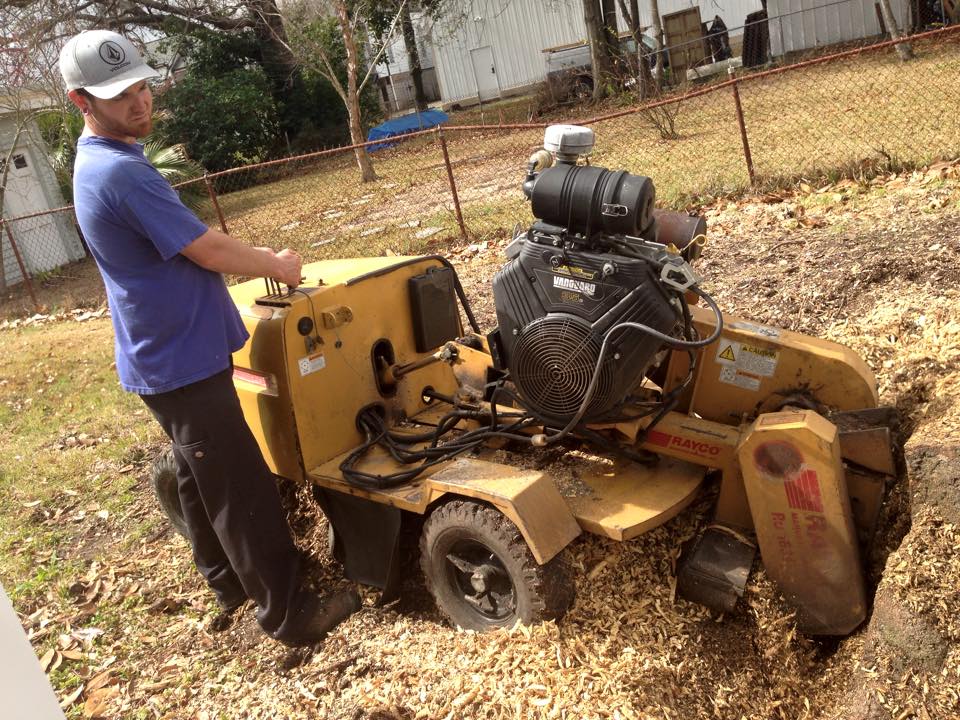 A man is working on a stump grinder in a yard