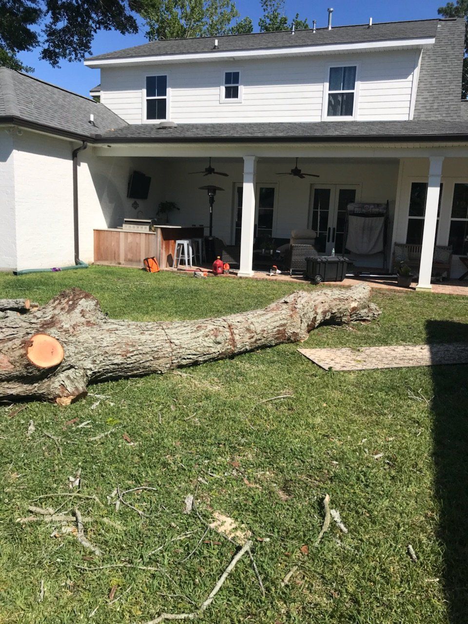A large log is laying in the grass in front of a house.