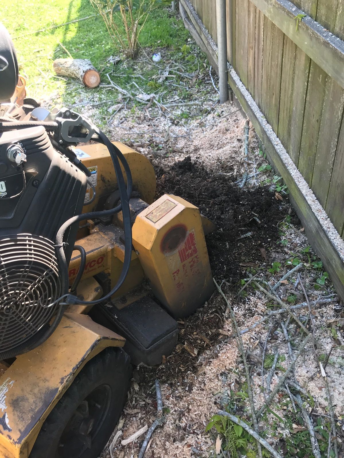 A stump grinder is sitting next to a wooden fence.