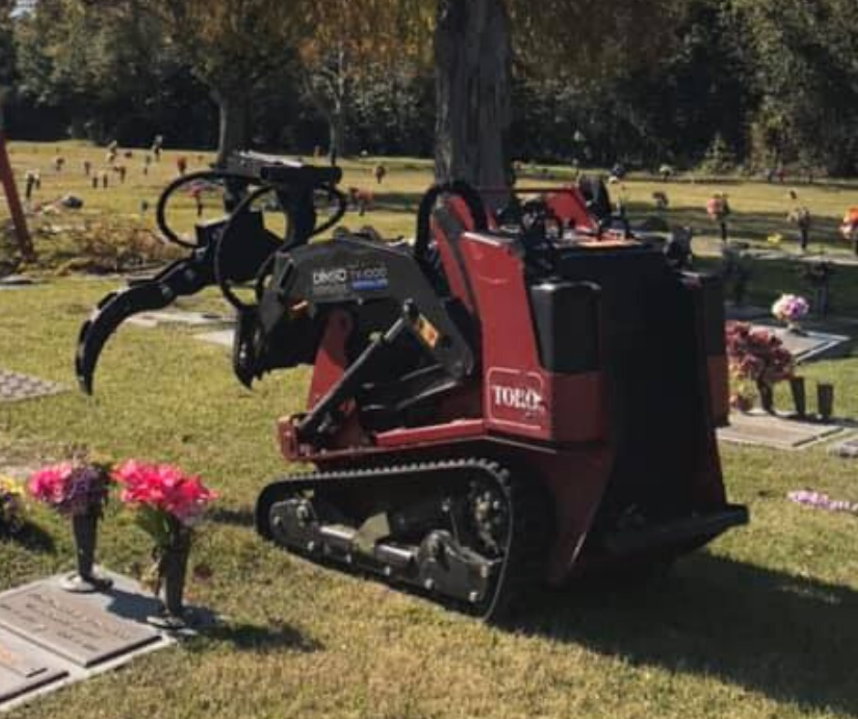 A red tractor is parked in a cemetery next to a tree. Tree Service Metairie LA