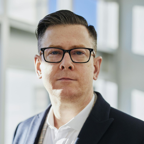 An older man with a beard is smiling in a black and white photo.