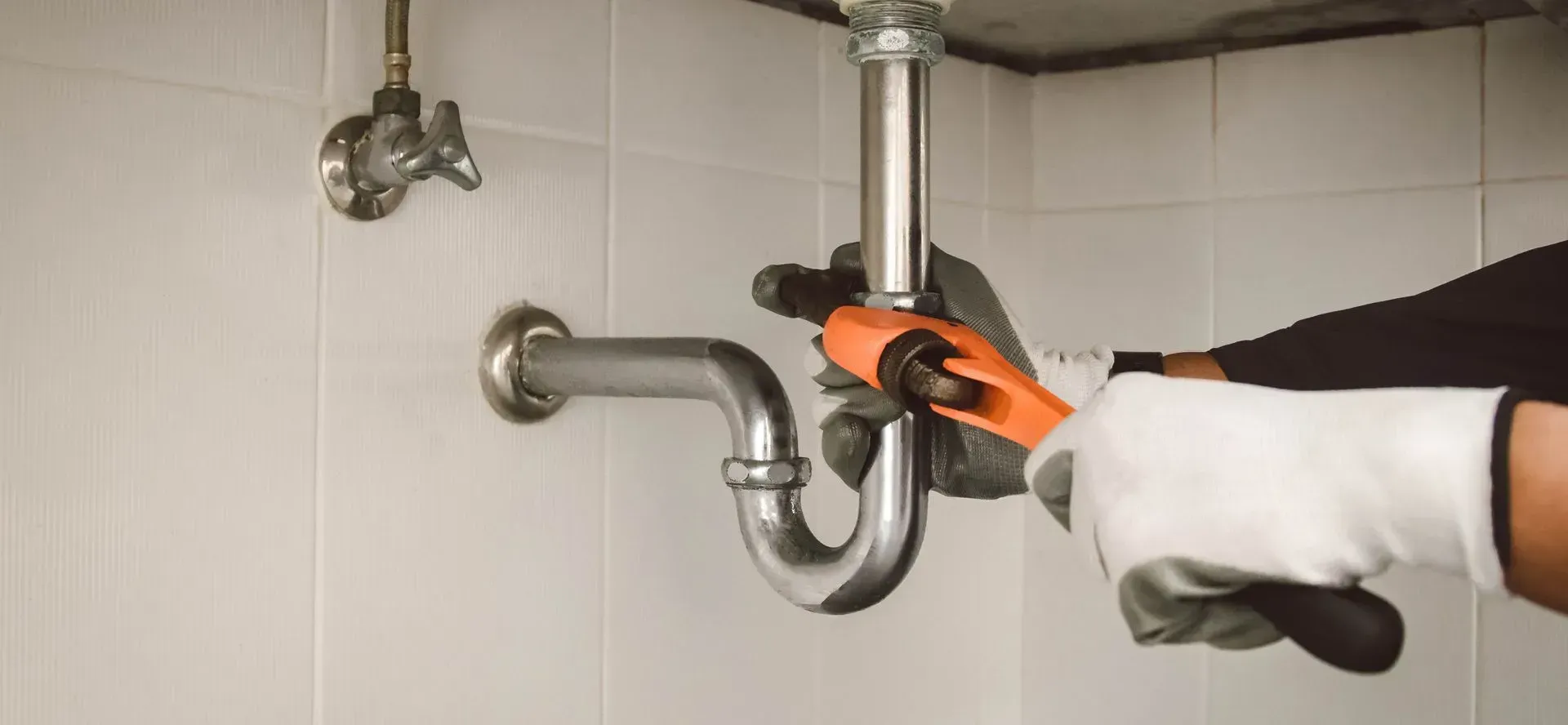 A plumber is fixing a sink pipe with a wrench.