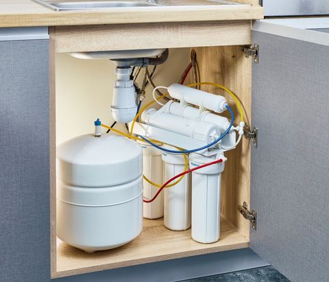 A water filter is sitting under a sink in a cabinet.
