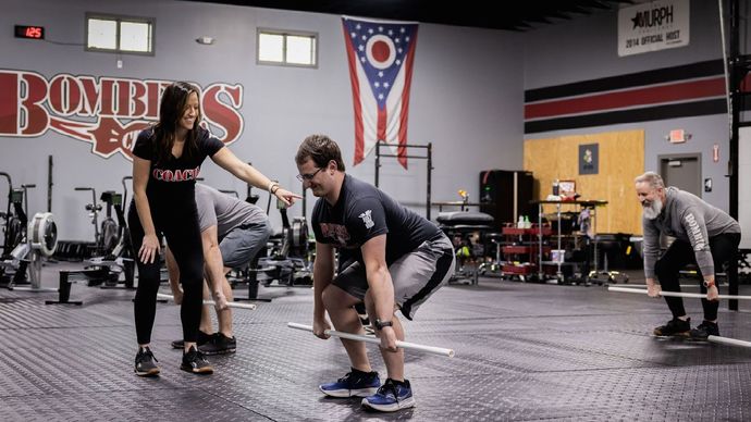 A woman is helping a man lift a barbell in a gym.