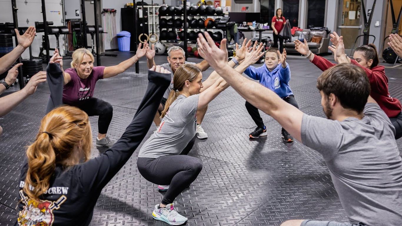 A group of people are squatting in a circle in a gym.