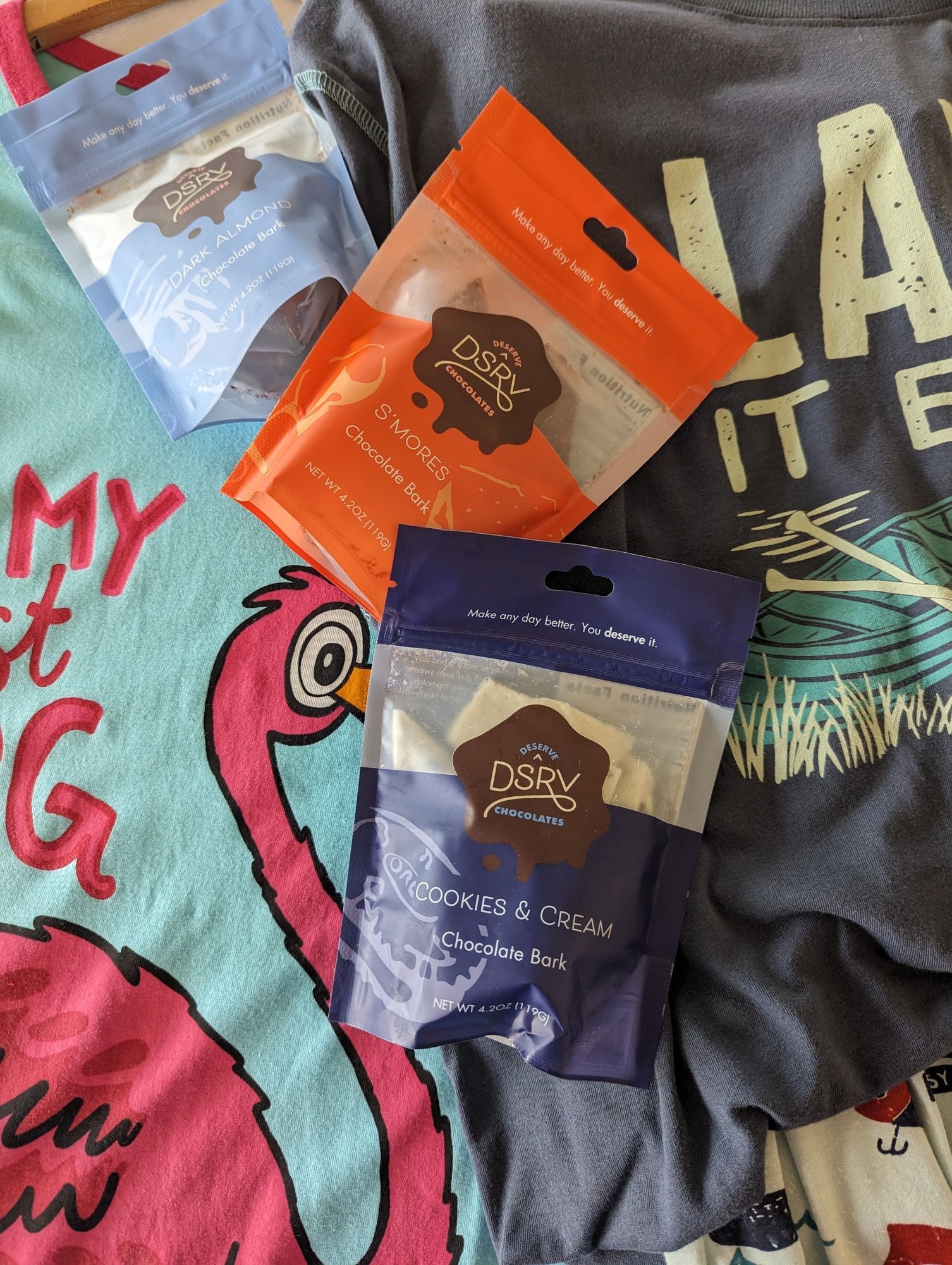 Three bags of chocolate are sitting on top of a flamingo t-shirt.