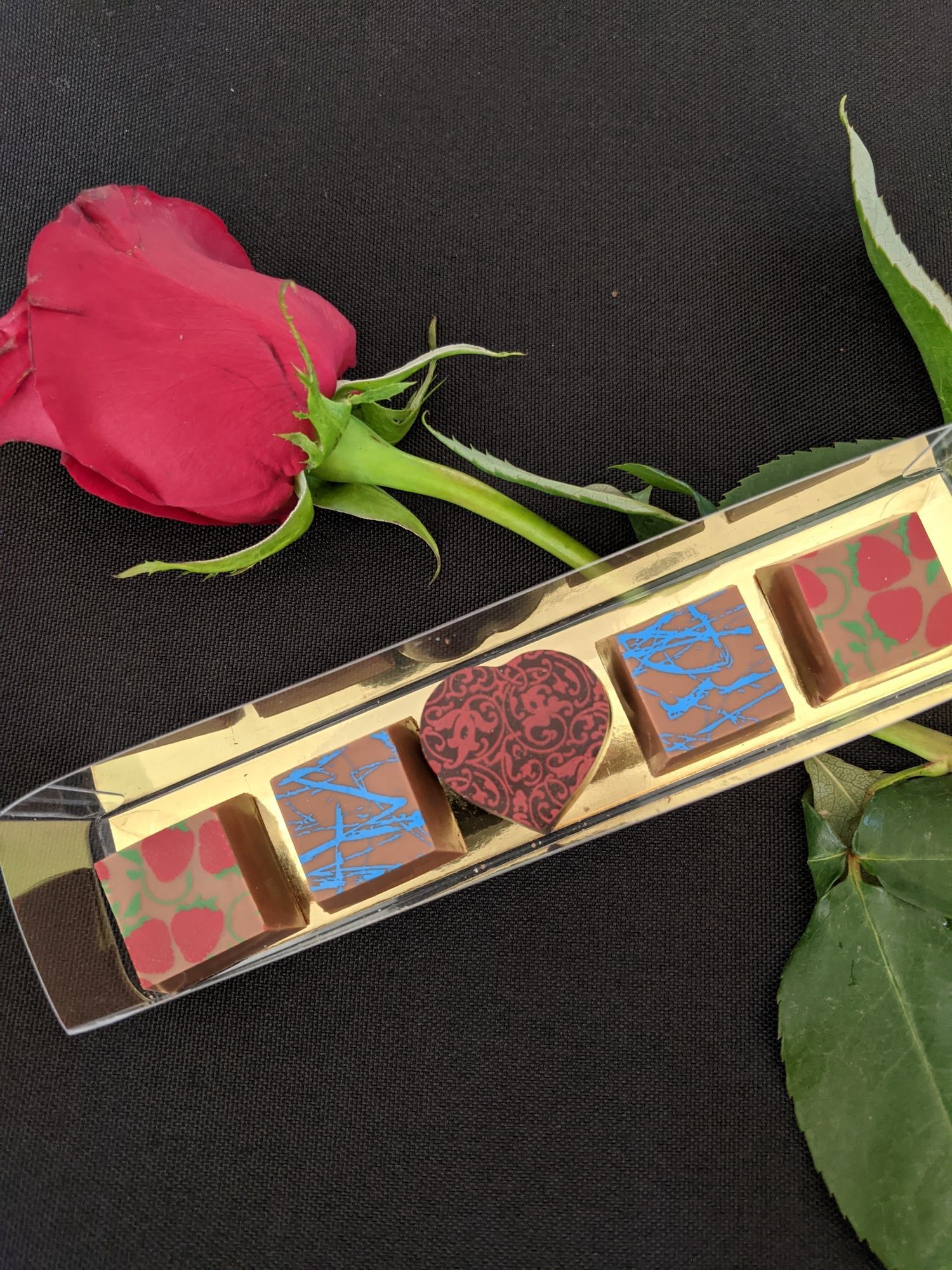 A box of chocolates with a heart on it next to a rose.