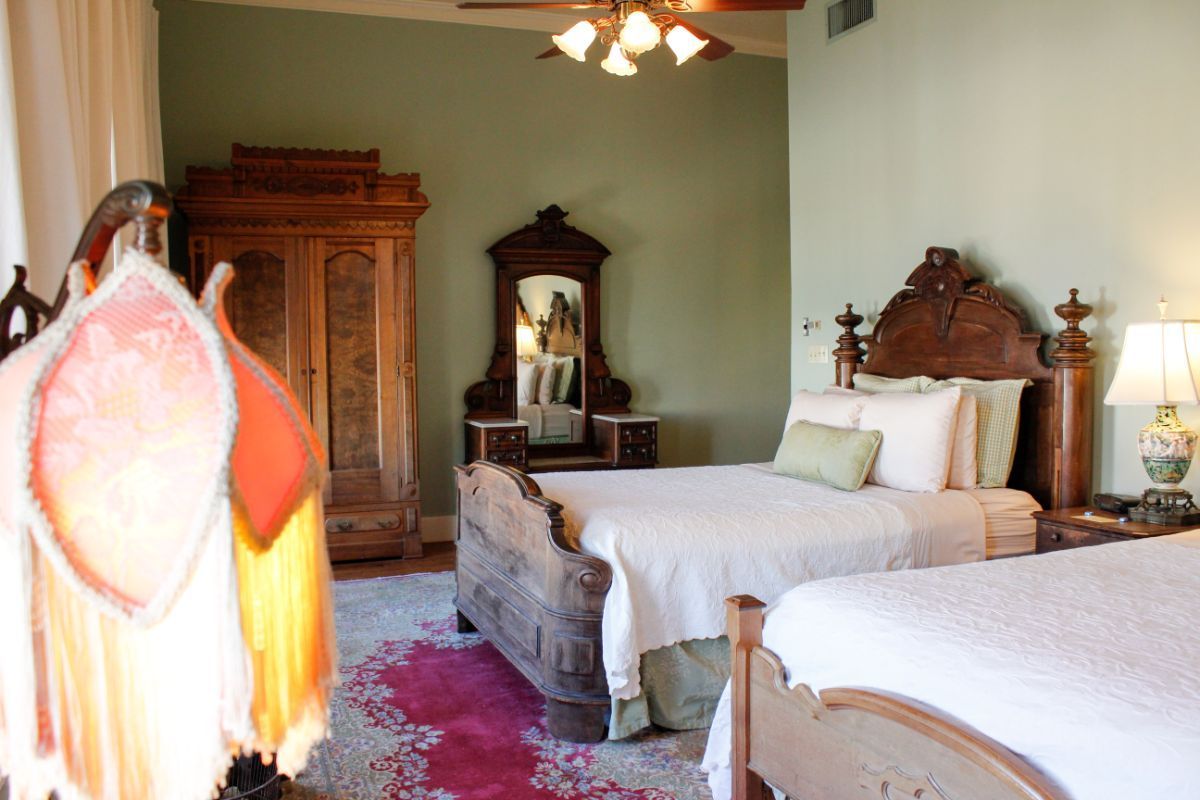 A bedroom with two beds , a dresser , a mirror and a ceiling fan.