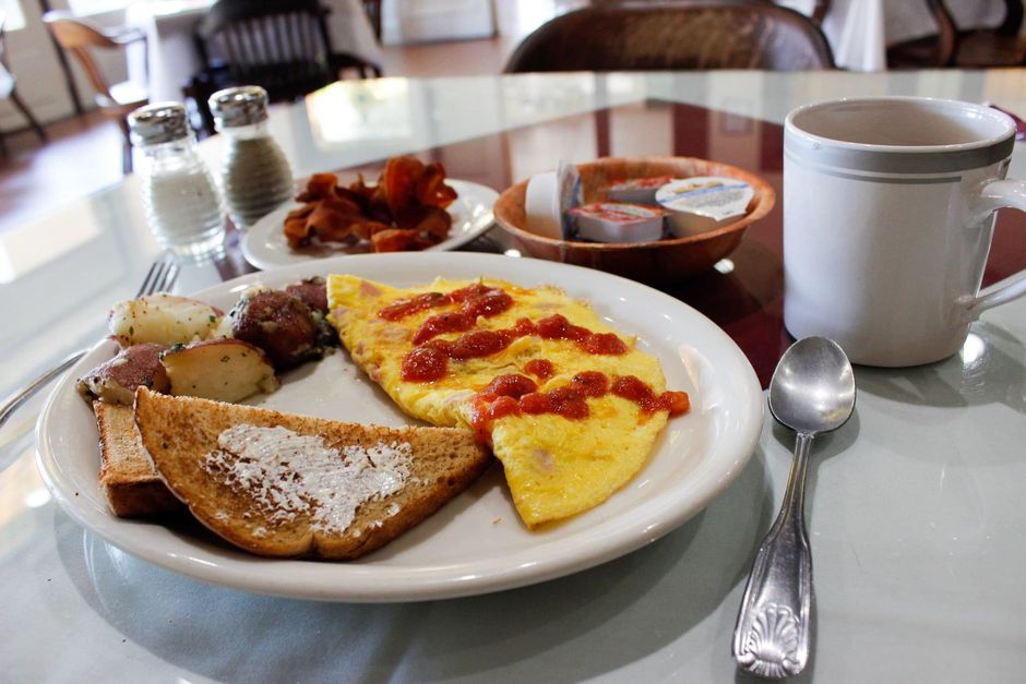 A plate of food with an omelet , toast , potatoes and a cup of coffee on a table.