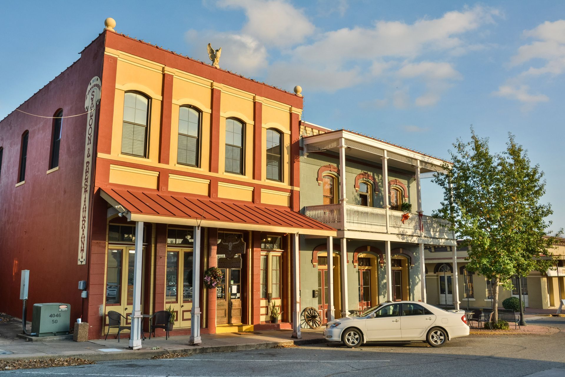A white car is parked in front of a row of buildings