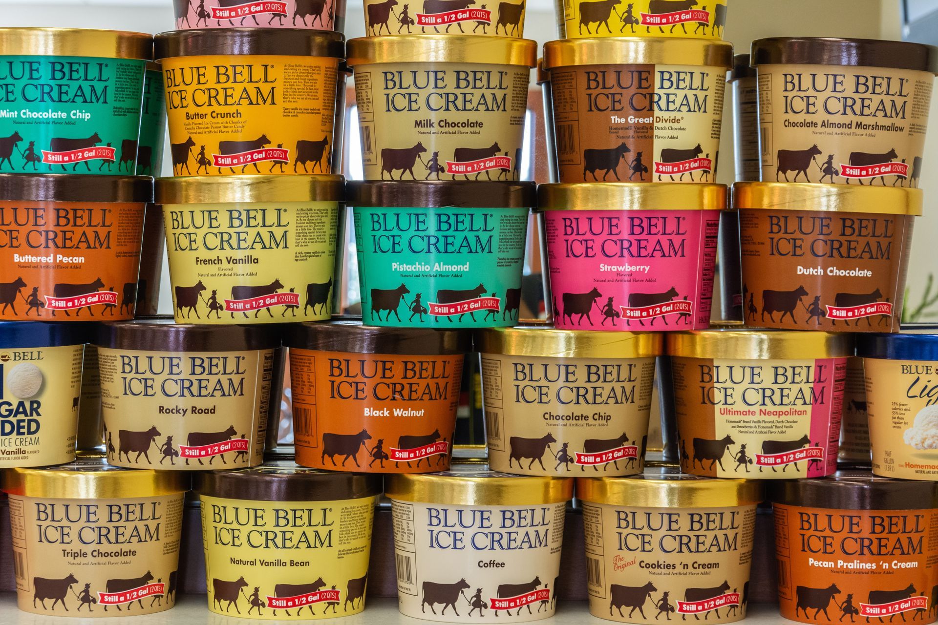 Many different flavors of blue bell ice cream are lined up on a shelf