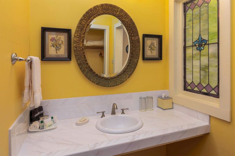 A bathroom with a sink , mirror and stained glass window.