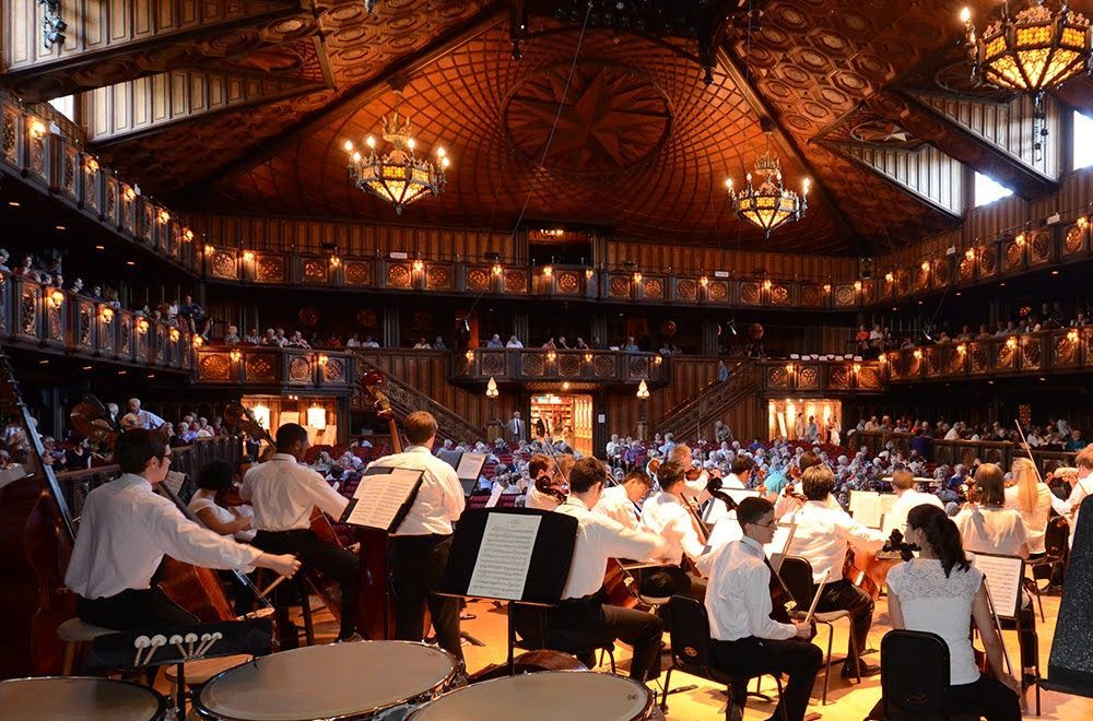 A large orchestra of students are playing in a large auditorium at round top festival institute