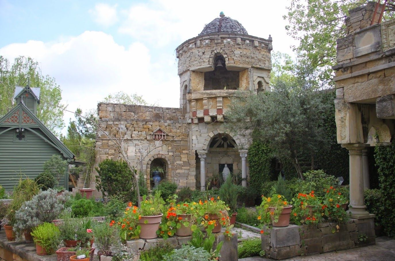 A large stone building with a dome on top of it is surrounded by potted plants and trees known as the herb garden