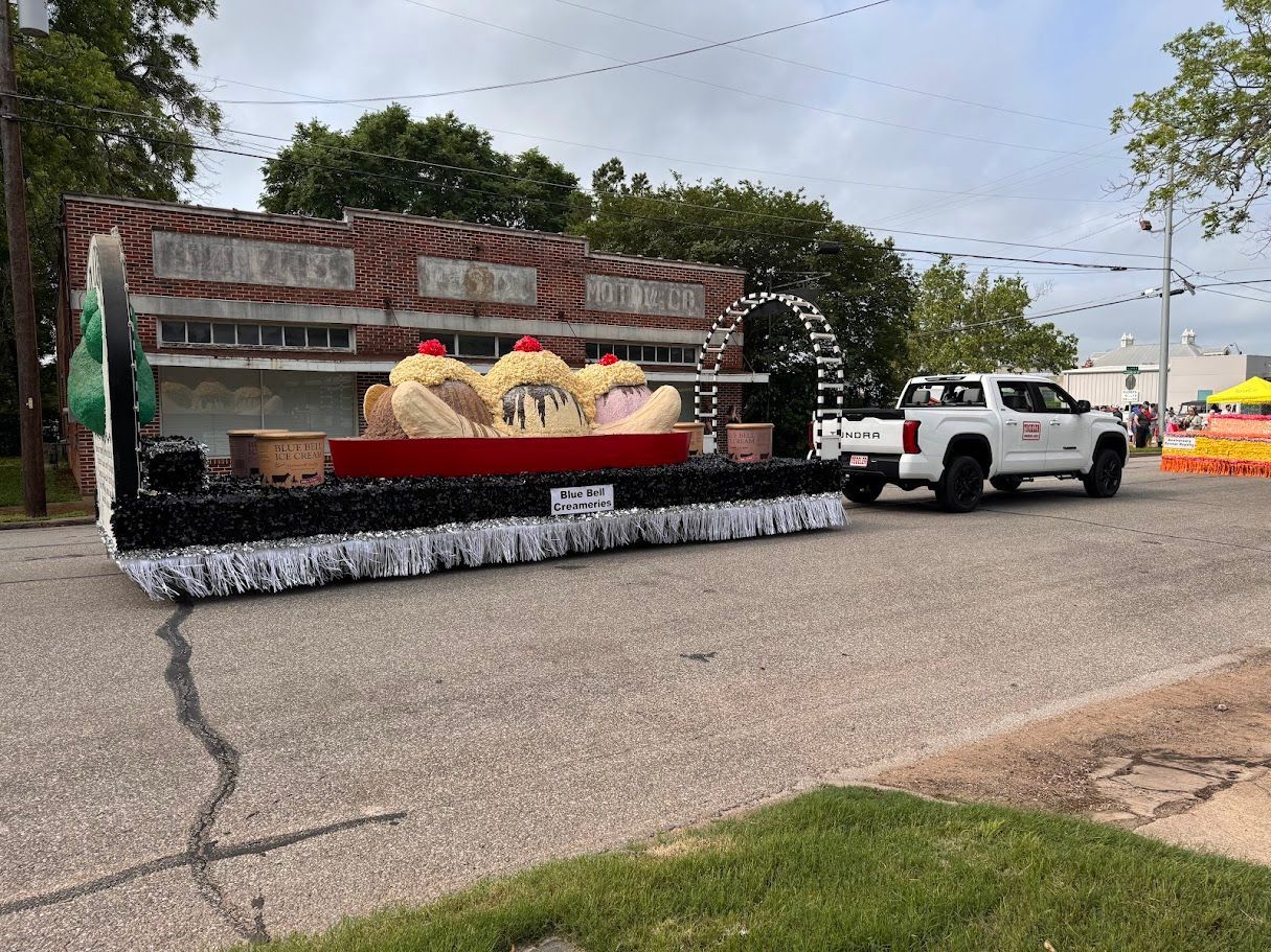 A parade float shaped like an ice cream shop with oversized ice cream scoops, pulled by a white truck.