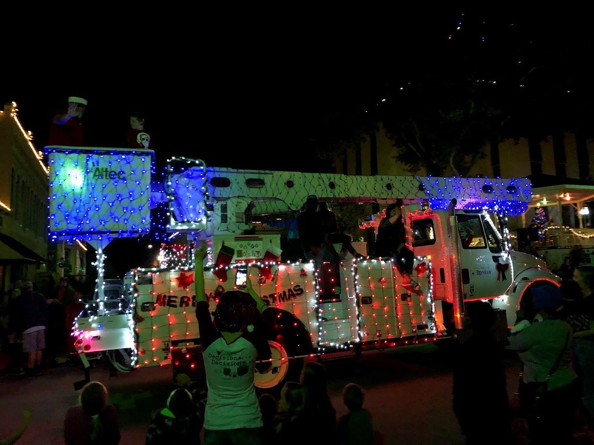 Fire truck decorated with Christmas lights in a nighttime parade, Santa waves from the top.