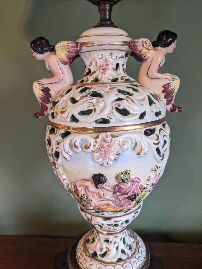 Ornate ceramic lamp with cherub figures, featuring hand-painted scenes and floral details.