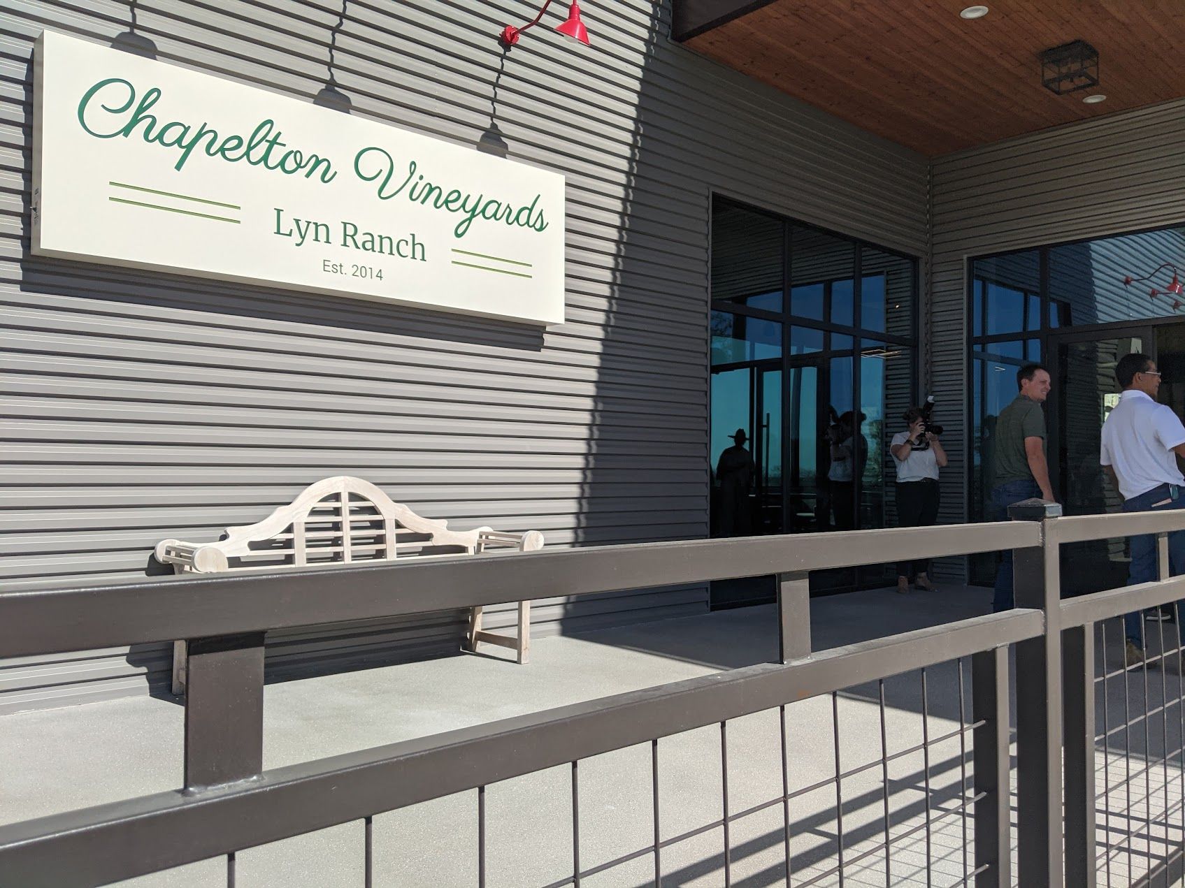 Chapelton Vineyards building with sign. People stand outside near a metal fence, sunny day.