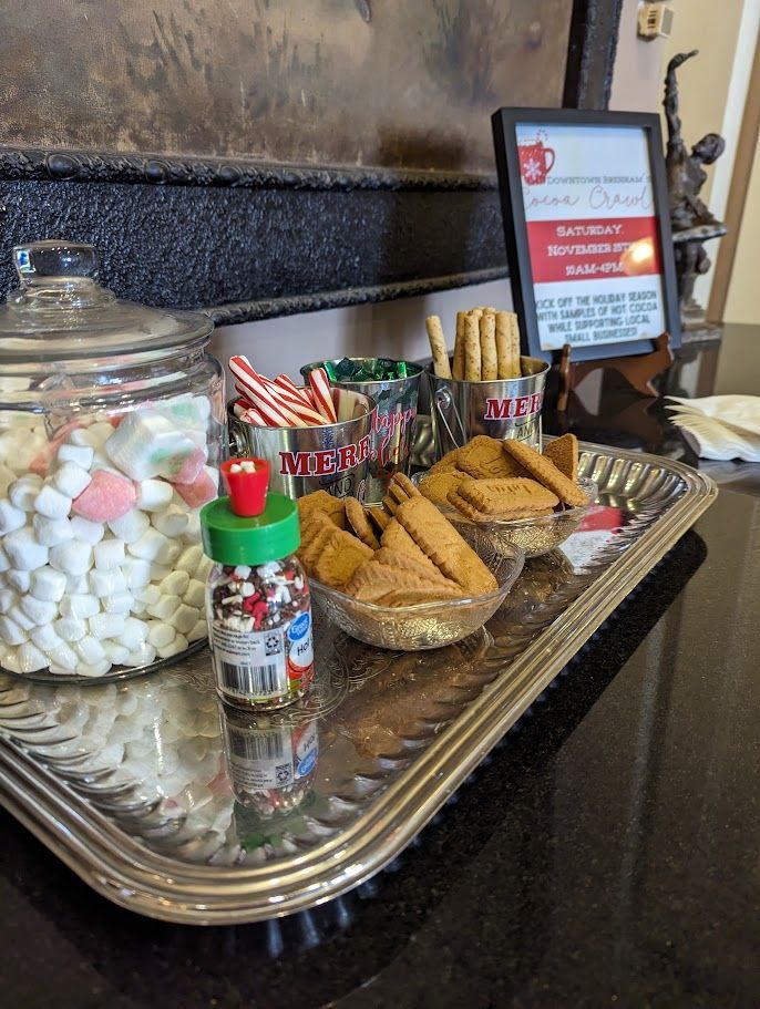 A silver tray holds hot chocolate toppings: marshmallows, candy canes, sprinkles, cookies, and biscotti.