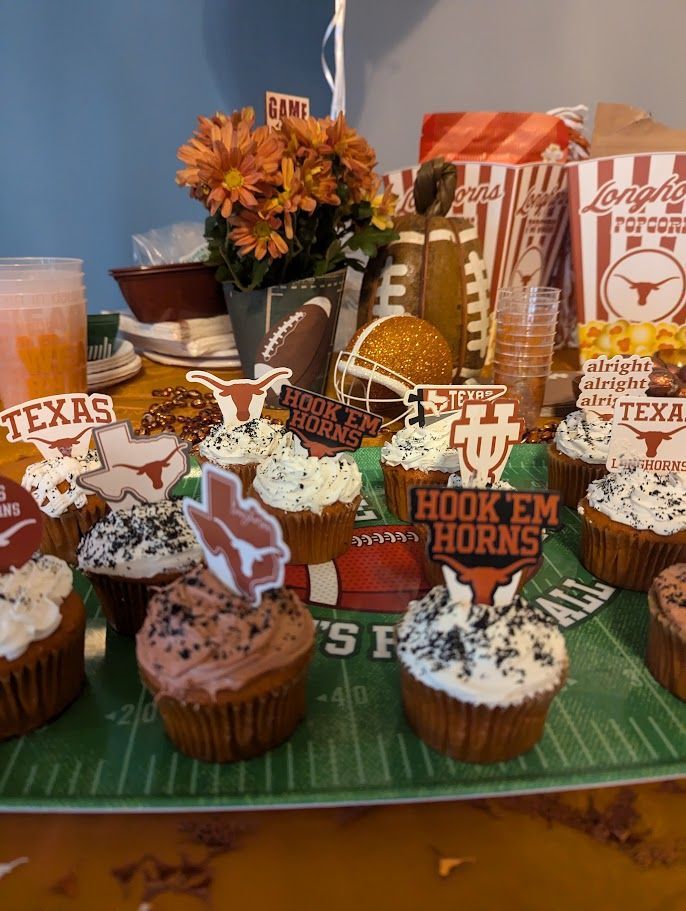 A table topped with cupcakes and a sign that says hook em horns