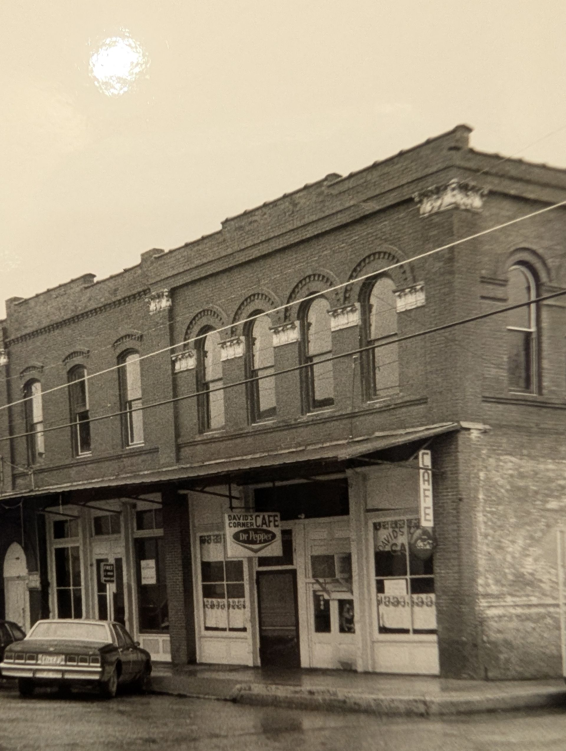Brick building with awnings over storefronts, a vintage car parked, and overcast sky.